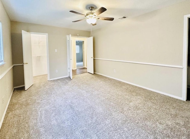 unfurnished bedroom with a walk in closet, ceiling fan, a closet, and light carpet