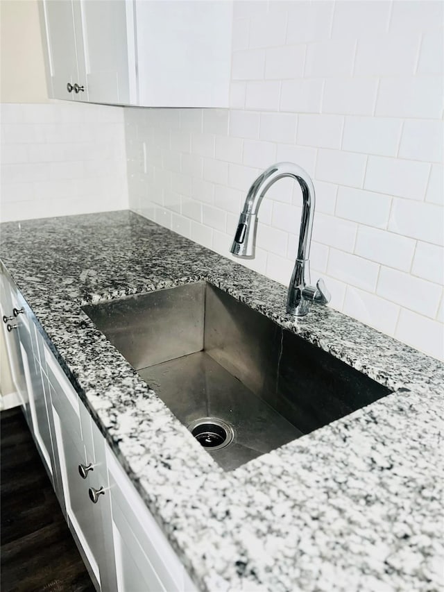 interior details with sink, dark wood-type flooring, tasteful backsplash, dark stone counters, and white cabinets