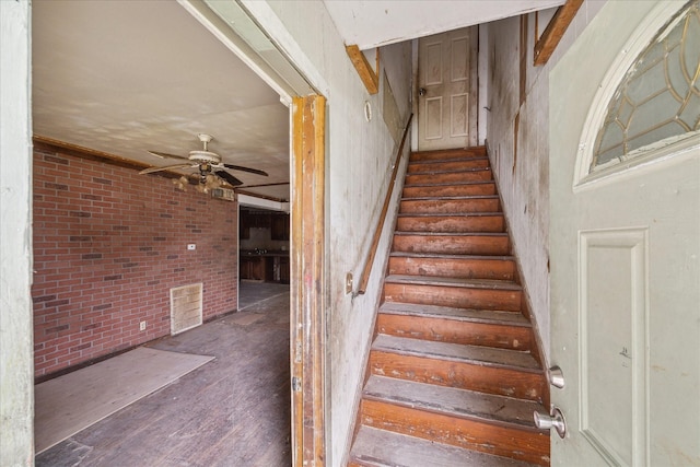 staircase with ceiling fan and brick wall