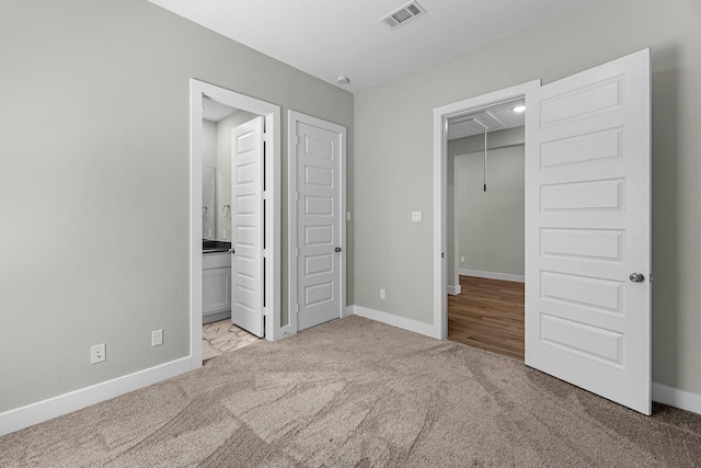 unfurnished bedroom with connected bathroom, a walk in closet, a closet, and light colored carpet