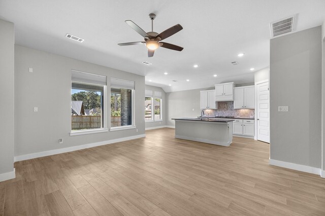 kitchen with white cabinetry, ceiling fan, light hardwood / wood-style flooring, an island with sink, and decorative backsplash