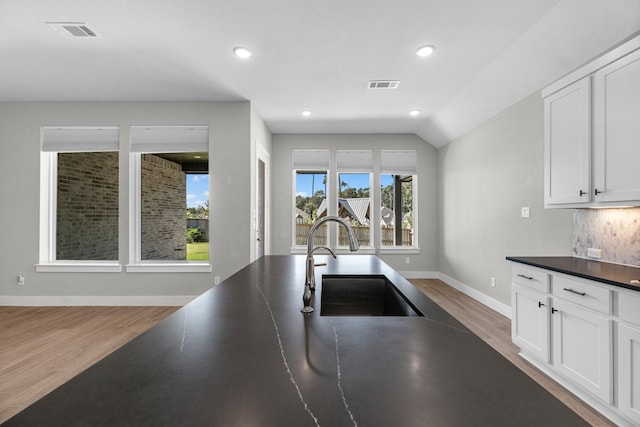 kitchen with decorative backsplash, sink, wood-type flooring, white cabinetry, and lofted ceiling