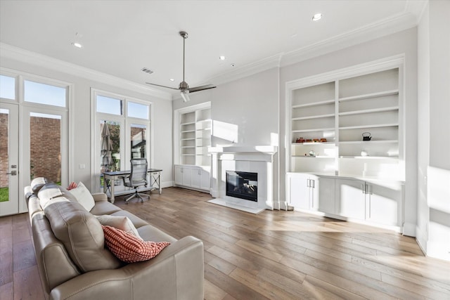 living room with built in shelves, ceiling fan, hardwood / wood-style flooring, and ornamental molding