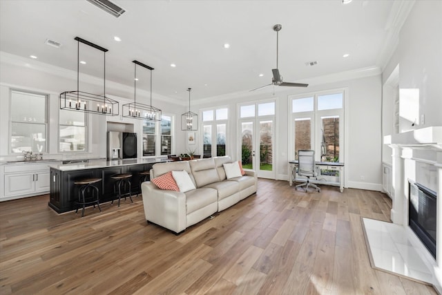 living room featuring a tiled fireplace, ceiling fan, ornamental molding, and light wood-type flooring