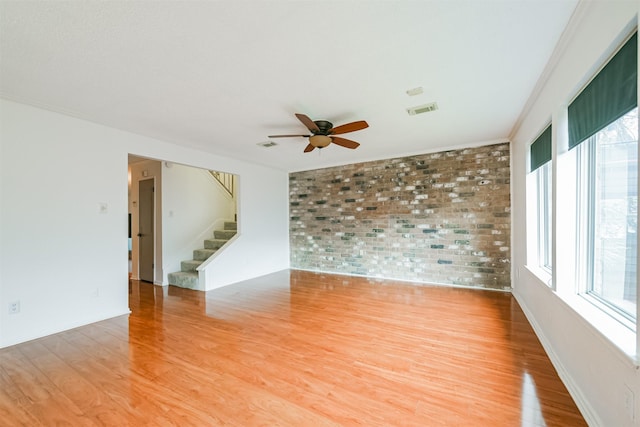 unfurnished room featuring ceiling fan, wood-type flooring, crown molding, and brick wall