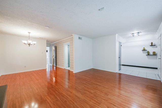 empty room featuring light hardwood / wood-style floors, ornamental molding, a textured ceiling, and a chandelier