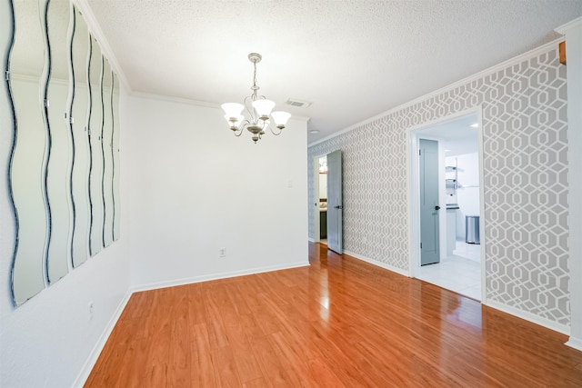 unfurnished room featuring a chandelier, light hardwood / wood-style floors, a textured ceiling, and ornamental molding