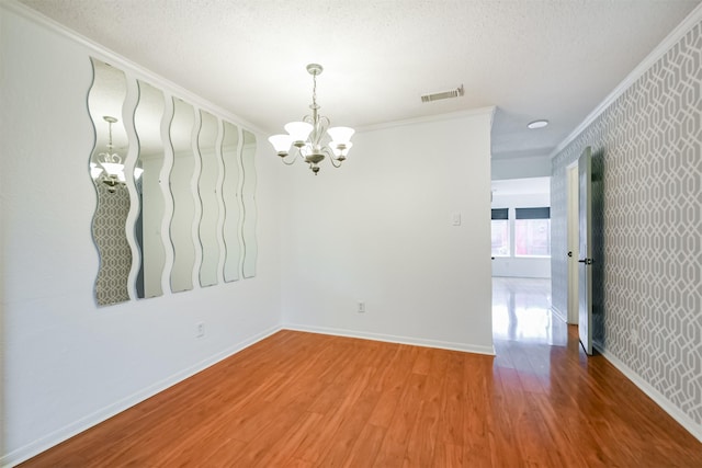 empty room featuring hardwood / wood-style flooring, a textured ceiling, crown molding, and an inviting chandelier