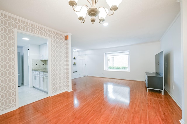 unfurnished living room with an inviting chandelier, light hardwood / wood-style flooring, and crown molding