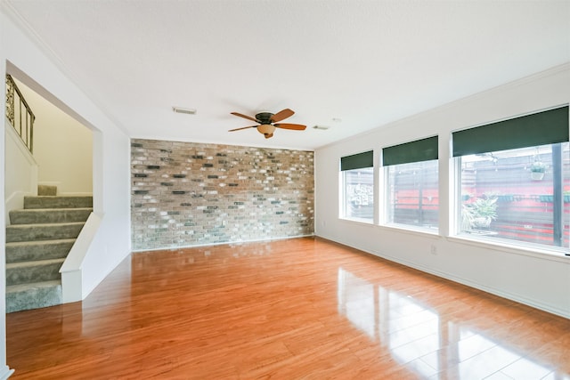 empty room featuring light wood-type flooring, ceiling fan, ornamental molding, and brick wall