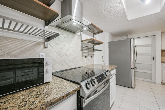 kitchen with a textured ceiling, stainless steel appliances, wall chimney exhaust hood, and light tile patterned flooring