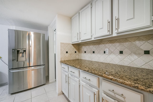 kitchen featuring backsplash, dark stone counters, light tile patterned floors, stainless steel fridge with ice dispenser, and white cabinetry