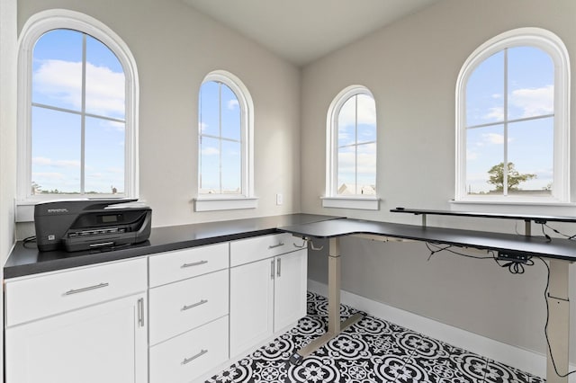 kitchen featuring a healthy amount of sunlight, light tile patterned flooring, lofted ceiling, white cabinets, and built in desk