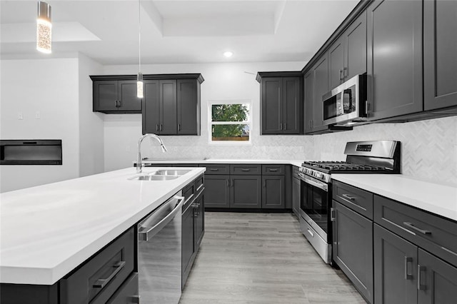 kitchen featuring pendant lighting, a raised ceiling, sink, light wood-type flooring, and stainless steel appliances