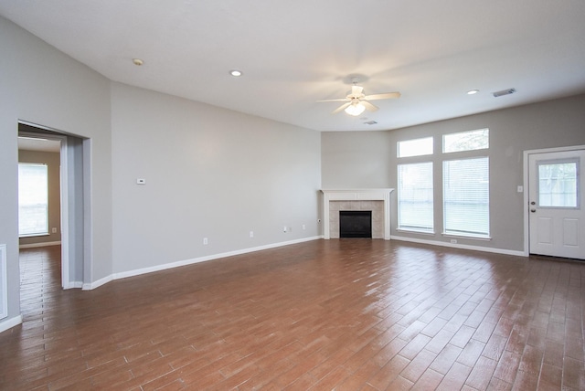 unfurnished living room featuring a tile fireplace, ceiling fan, and dark hardwood / wood-style flooring