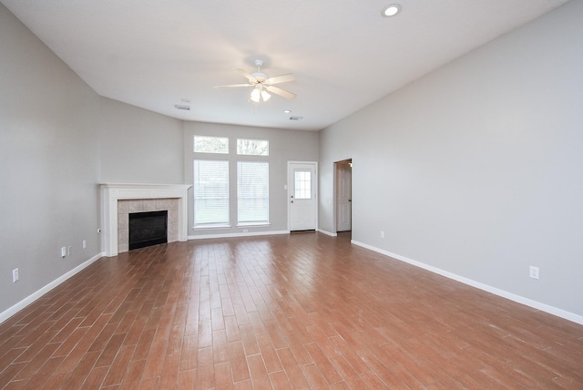 unfurnished living room with a tiled fireplace, ceiling fan, and hardwood / wood-style floors