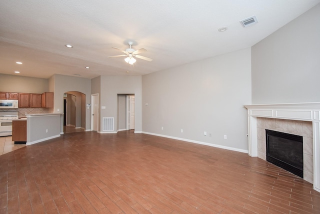 unfurnished living room featuring light hardwood / wood-style floors, ceiling fan, and a tiled fireplace