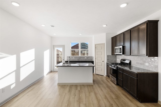 kitchen featuring stainless steel appliances, sink, light hardwood / wood-style flooring, an island with sink, and dark stone counters