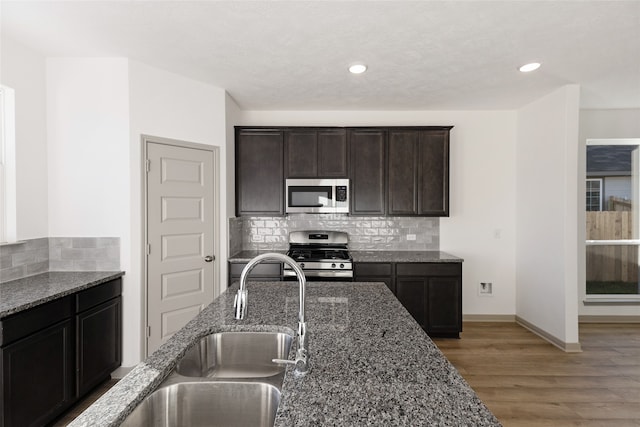 kitchen featuring tasteful backsplash, stone countertops, appliances with stainless steel finishes, wood-type flooring, and dark brown cabinetry