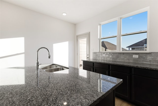 kitchen featuring sink, hardwood / wood-style flooring, tasteful backsplash, dark stone counters, and a center island with sink