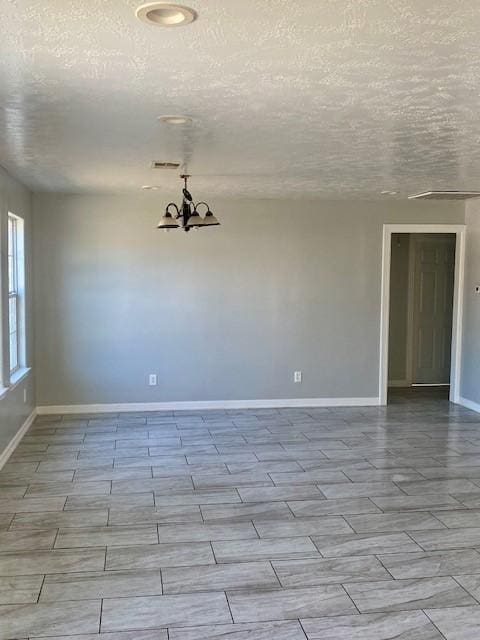 empty room featuring a textured ceiling and a notable chandelier