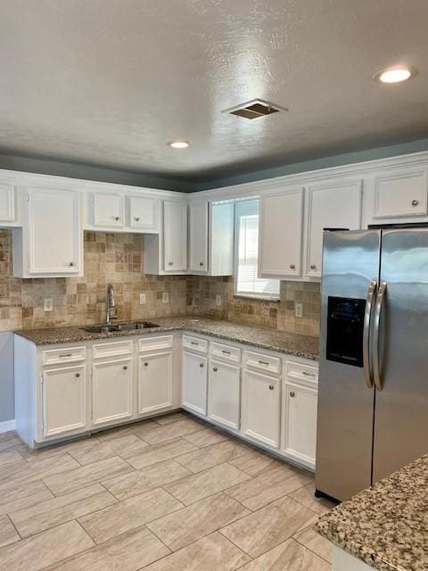 kitchen with white cabinets, stainless steel fridge with ice dispenser, stone counters, and sink