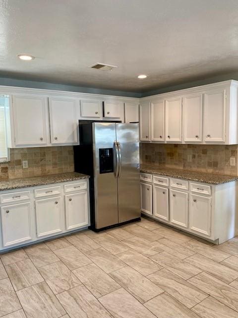 kitchen with white cabinets, stainless steel refrigerator with ice dispenser, decorative backsplash, and light stone counters