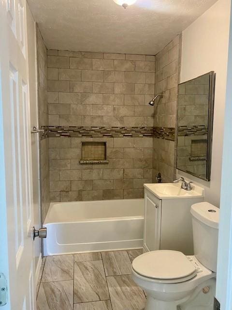 full bathroom featuring a textured ceiling, vanity, toilet, and tiled shower / bath