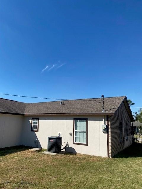 back of property featuring a lawn and central air condition unit