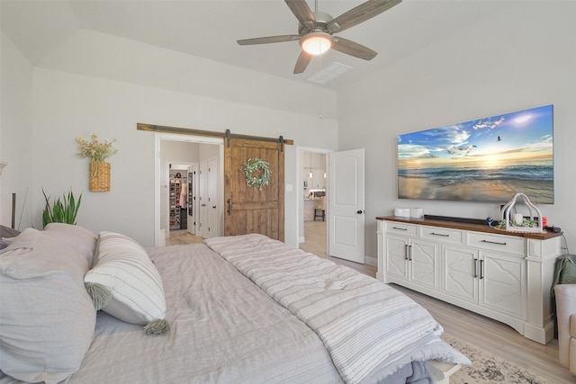 bedroom with a spacious closet, ceiling fan, a barn door, light hardwood / wood-style flooring, and a closet