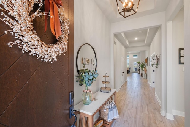 corridor with a tray ceiling, hardwood / wood-style floors, and a chandelier