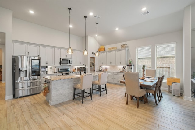 kitchen featuring stainless steel appliances, light stone counters, an island with sink, decorative light fixtures, and white cabinets