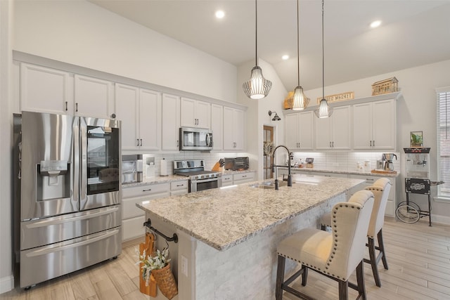 kitchen with a kitchen island with sink, sink, light stone counters, white cabinetry, and stainless steel appliances