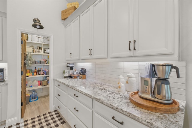 interior space featuring white cabinets, backsplash, light hardwood / wood-style flooring, and light stone counters