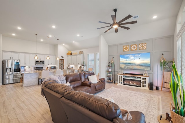 living room featuring ceiling fan, a high ceiling, and light hardwood / wood-style flooring