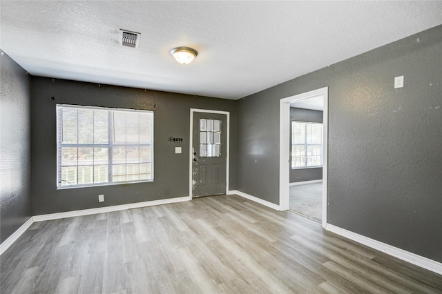 entrance foyer with light wood-type flooring, a textured ceiling, and a wealth of natural light