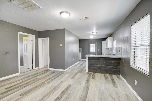 kitchen featuring white cabinetry, sink, kitchen peninsula, a textured ceiling, and light wood-type flooring