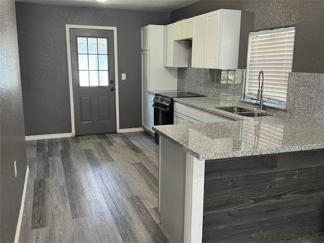 kitchen with sink, electric range, light stone countertops, white cabinetry, and kitchen peninsula