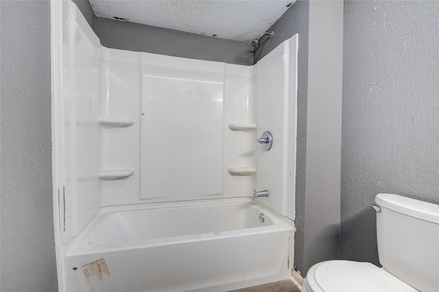 bathroom with washtub / shower combination, a textured ceiling, and toilet