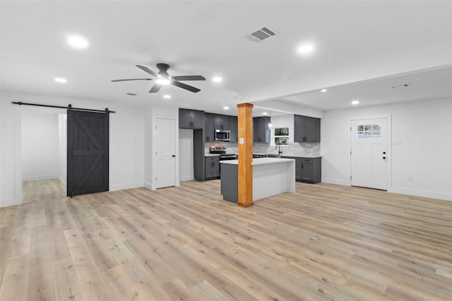 kitchen with ceiling fan, a center island, a barn door, light hardwood / wood-style flooring, and appliances with stainless steel finishes