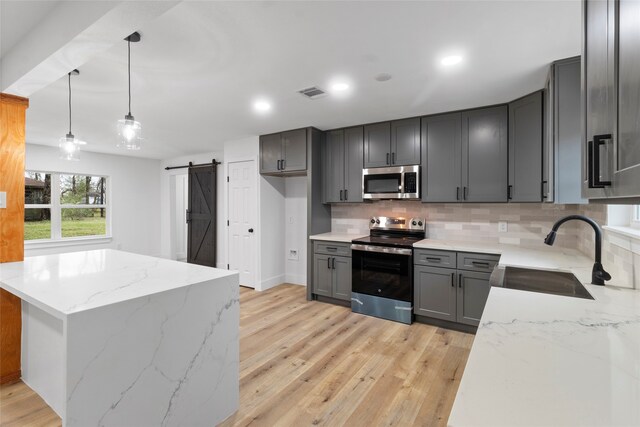 kitchen with sink, gray cabinets, a barn door, appliances with stainless steel finishes, and decorative light fixtures