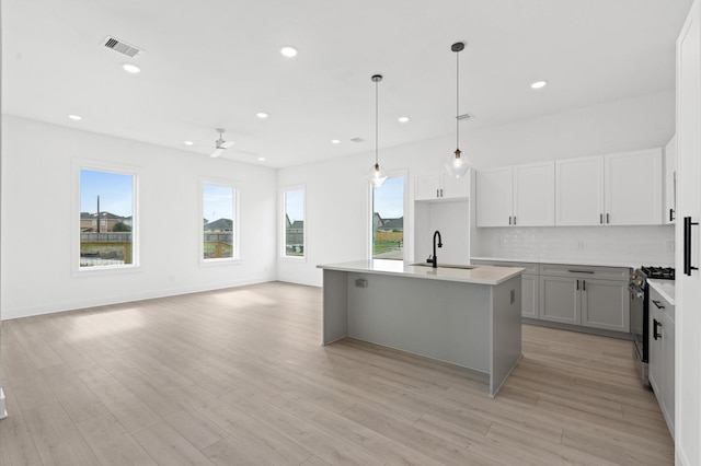 kitchen with ceiling fan, a kitchen island with sink, sink, pendant lighting, and stainless steel range with gas stovetop