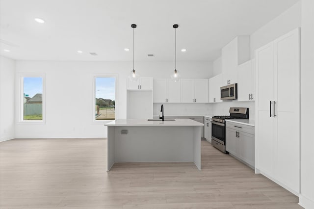 kitchen with sink, stainless steel appliances, an island with sink, pendant lighting, and white cabinets