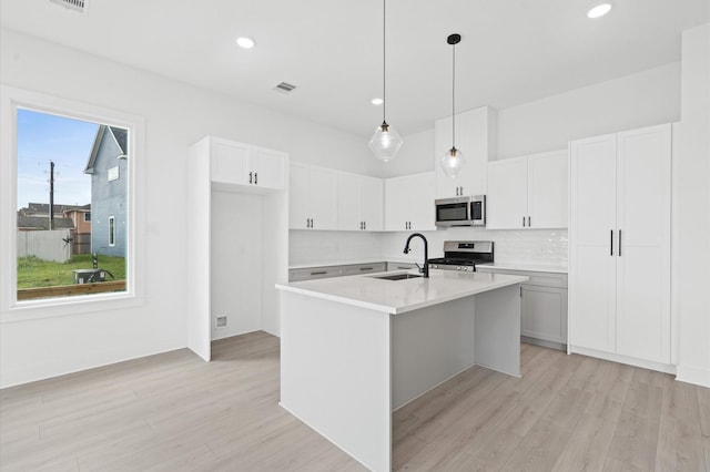 kitchen featuring stainless steel appliances, sink, pendant lighting, a center island with sink, and white cabinetry