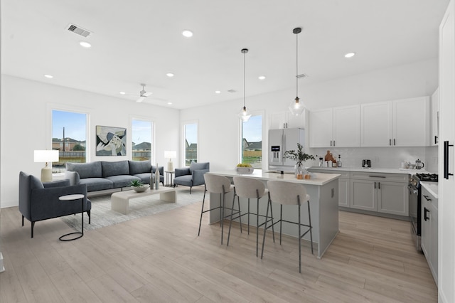 kitchen with ceiling fan, a center island, white fridge with ice dispenser, a kitchen breakfast bar, and stainless steel range with gas cooktop