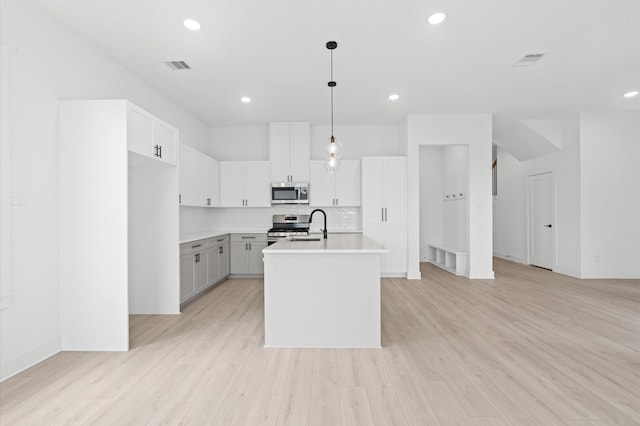 kitchen featuring stainless steel appliances, backsplash, decorative light fixtures, a kitchen island with sink, and white cabinets