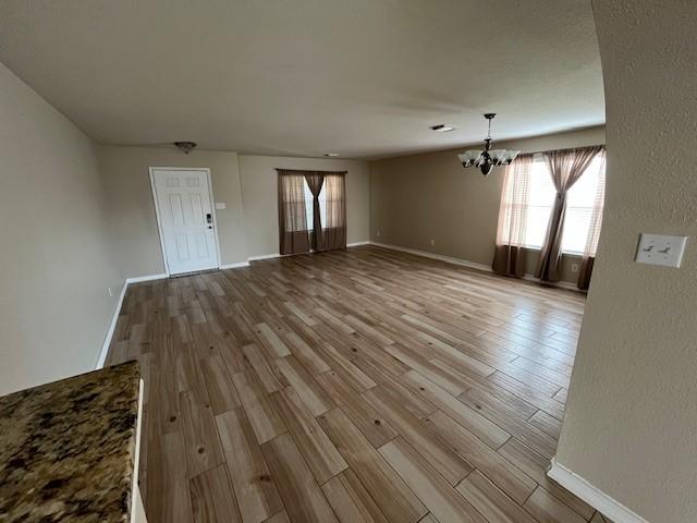 unfurnished living room featuring a notable chandelier and light hardwood / wood-style floors