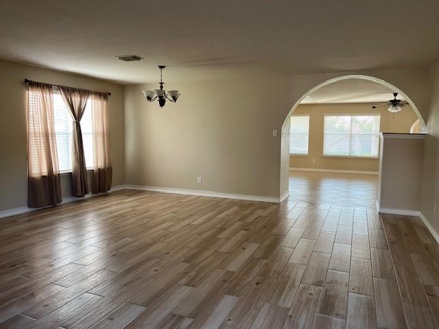 spare room with ceiling fan with notable chandelier and wood-type flooring