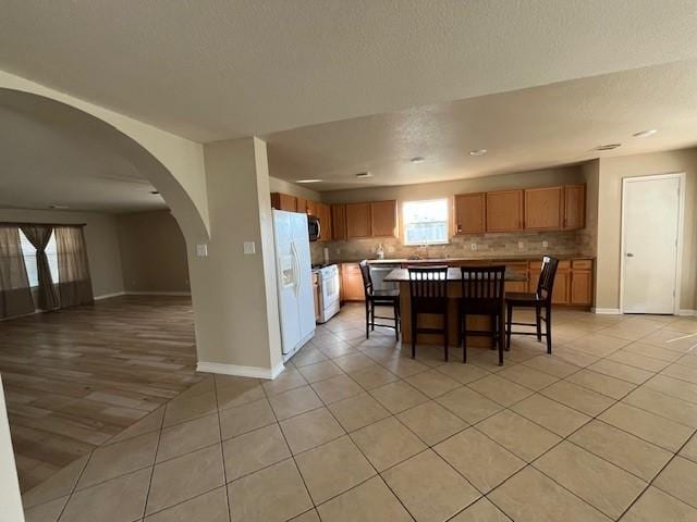 kitchen featuring a center island, a kitchen breakfast bar, white refrigerator with ice dispenser, stove, and light tile patterned floors