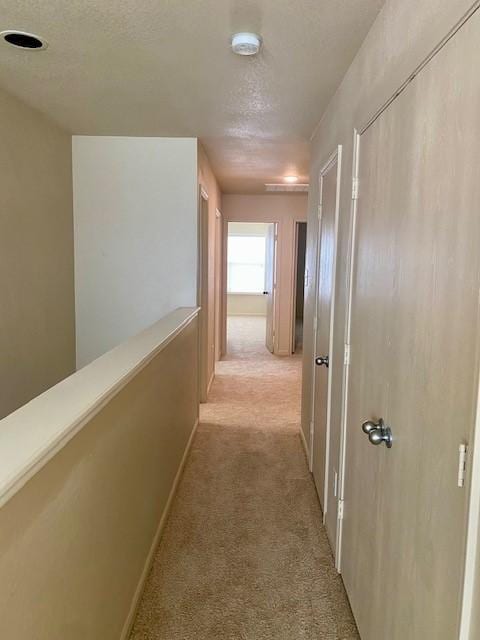 hall featuring light colored carpet and a textured ceiling